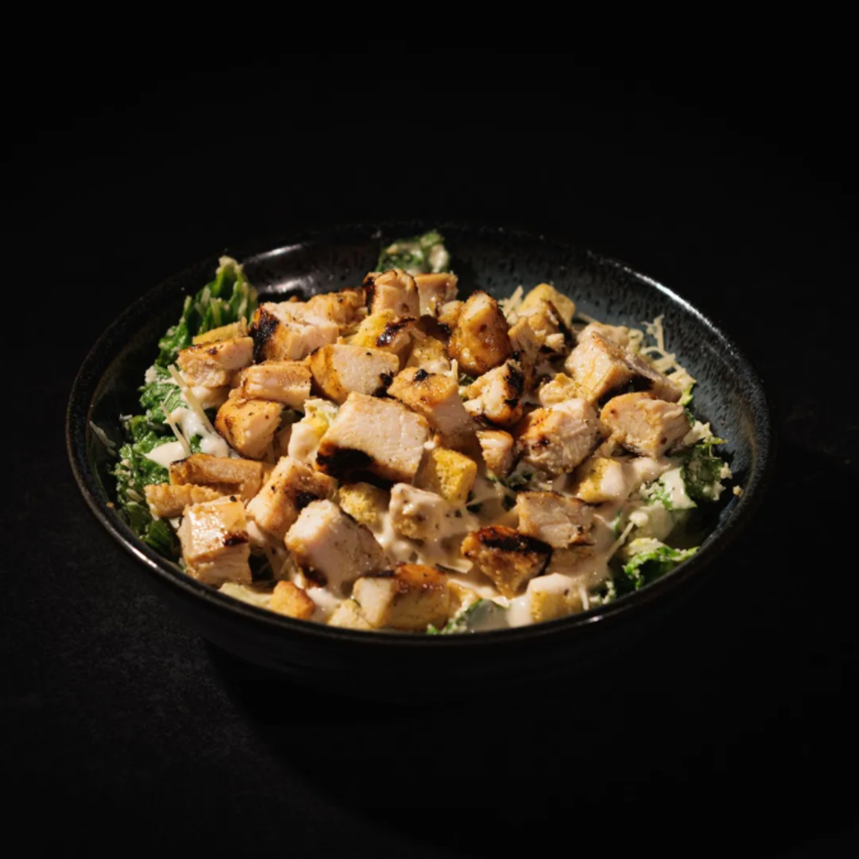 Chalet's Caesar salad with grilled chicken, croutons, and creamy dressing in a dark bowl.