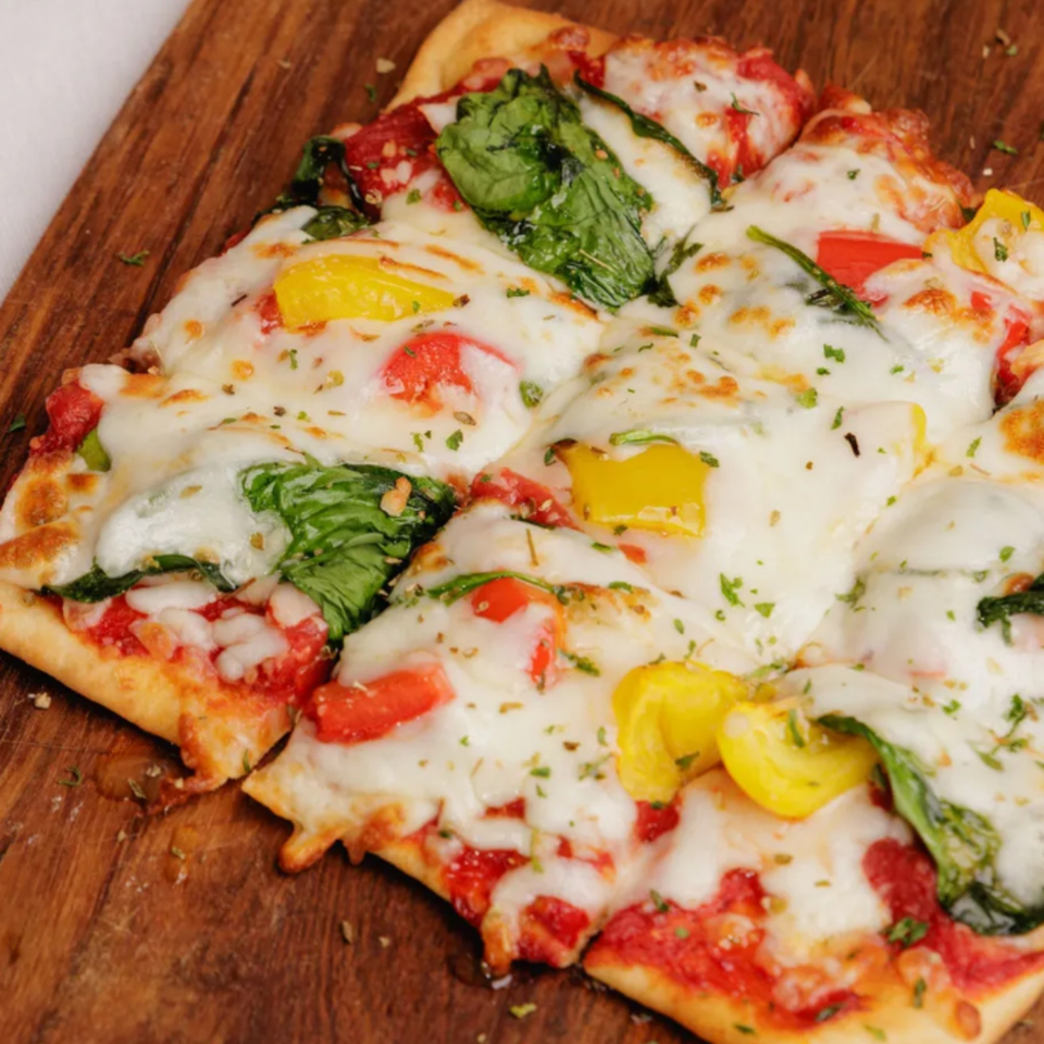 Chalet's American-style pizza with melted cheese, spinach, red and yellow bell peppers on a wooden board.