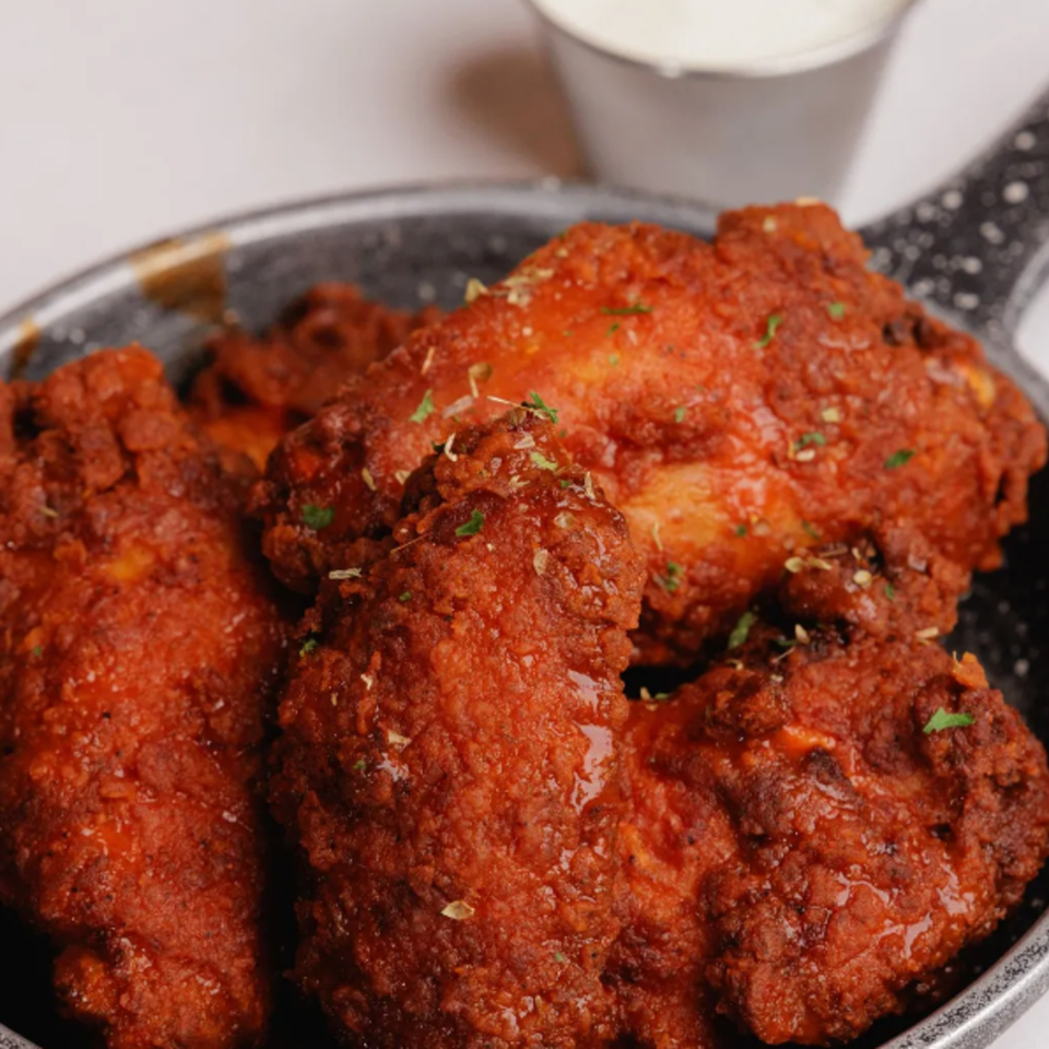 Close-up of Chalet's American-style chicken wings, coated in a vibrant red sauce and sprinkled with herbs.