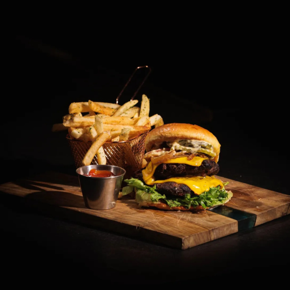 Double cheeseburger with lettuce, onions, and pickles, served with fries and ketchup on a wooden board.