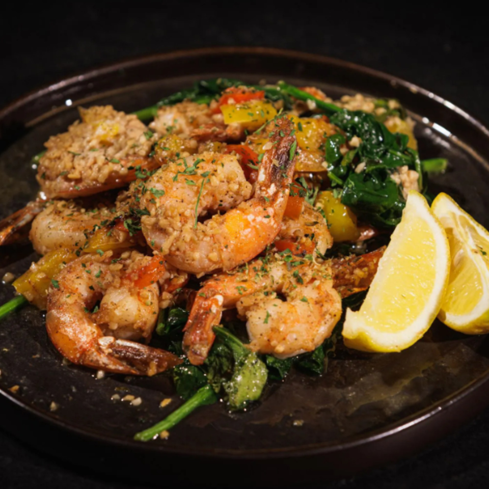 Garlic shrimp with spinach, bell peppers, and lemon wedges on a dark plate at Chalet.